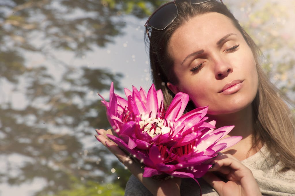 A beautiful woman with closed eyes holding pink lotus flowers in sunlight.