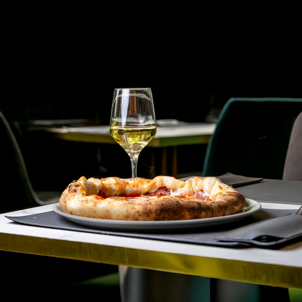 Gourmet pizza with white wine on a restaurant table, perfect for elegant dining experiences.
