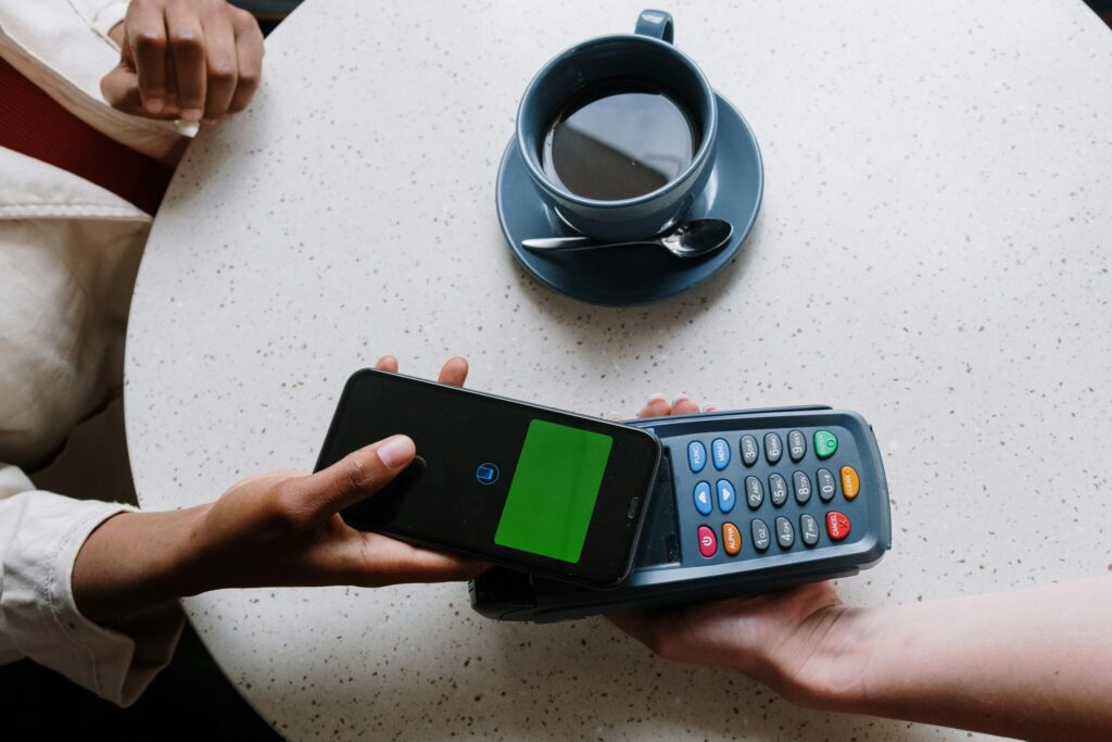 Contactless payment using a smartphone and card reader at a coffee shop table.