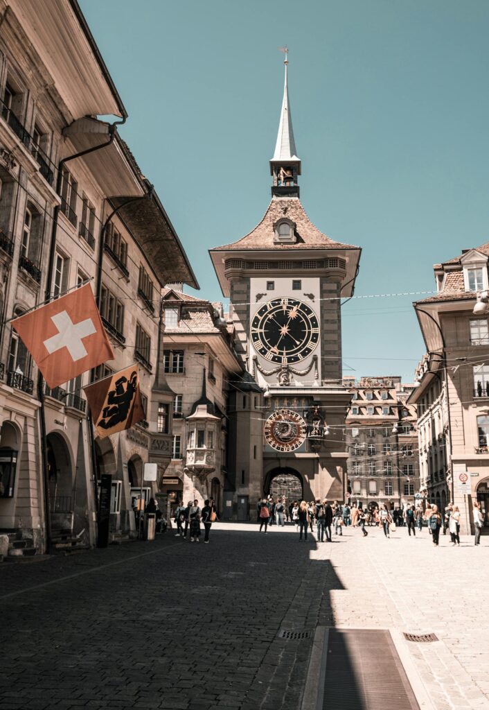 View of Bern's iconic Zytglogge clock tower with Swiss flags and tourists.