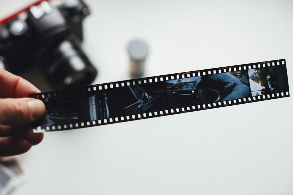 Close-up of a hand holding a vintage film strip with a blurred camera in the background, evoking nostalgia.