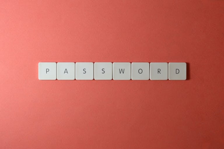 Focus on password security with white keyboard tiles spelling 'PASSWORD' on a coral background.