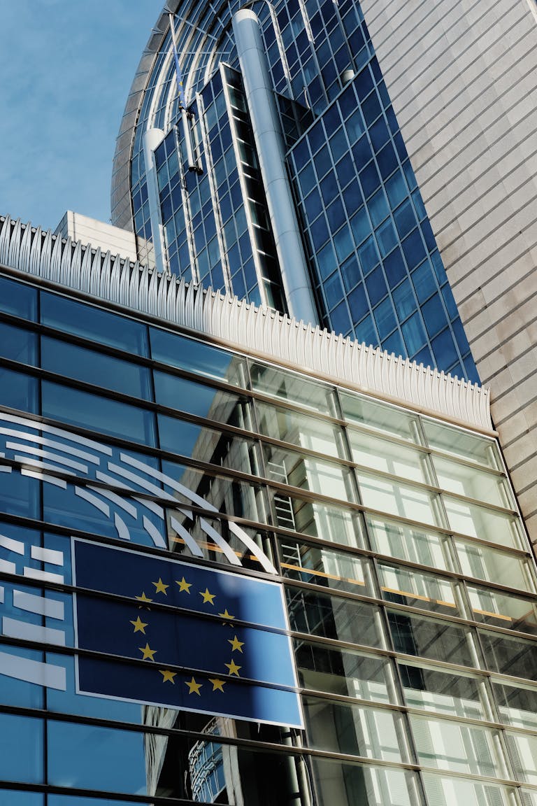 Low angle view of modern glass facade with EU flag at European Union Headquarters.