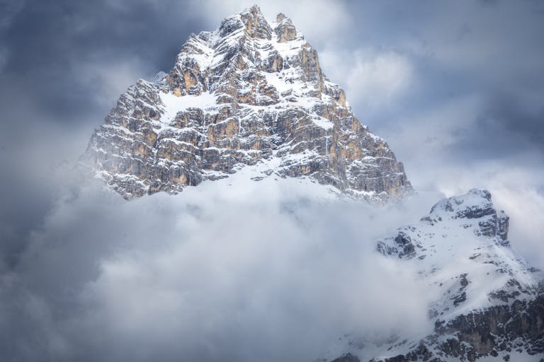 Majestic snow-covered peak in Cortina d'Ampezzo, Italy, surrounded by clouds.